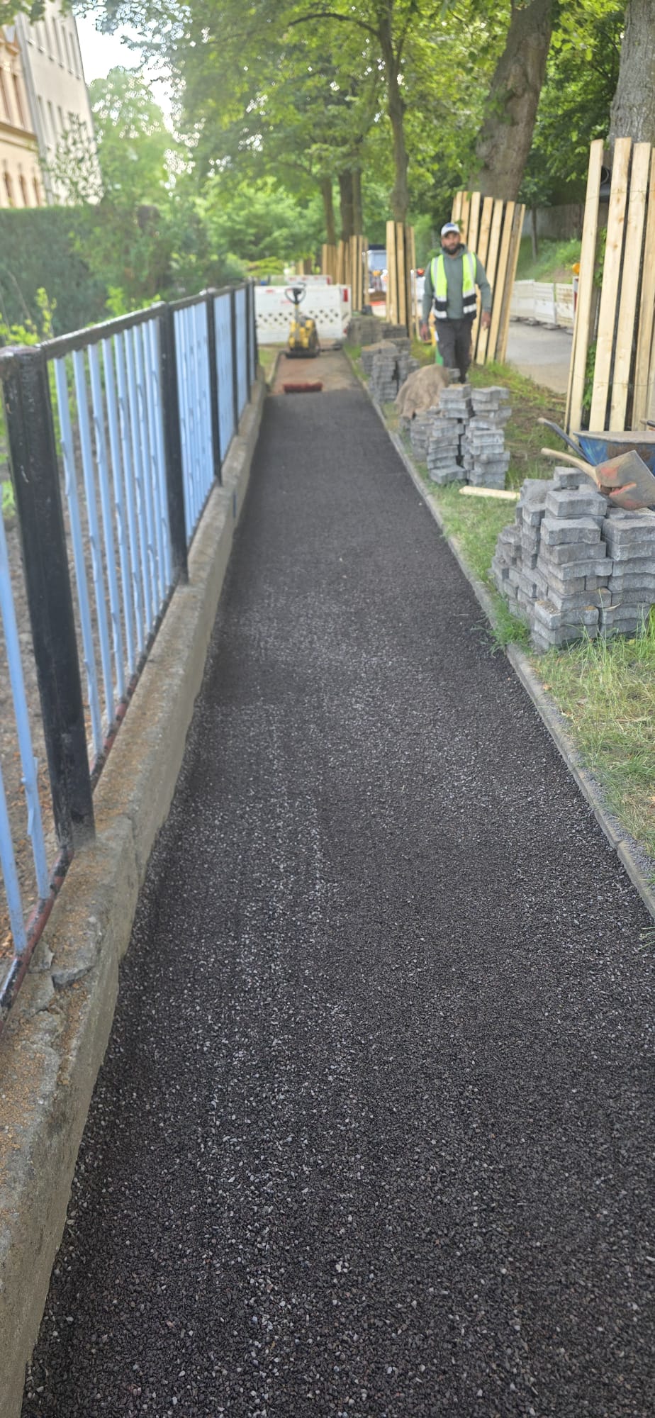Fertiggestellter Asphaltgehweg entlang eines Zauns